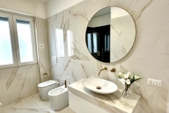Erretre Ceramiche realizzazione di un bagno moderno in una villetta a Magenta con pavimento e pareti rivestite con piastrelle chiare, con water, bidet e lavabo  di colore bianco e con specchio rotondo alla parete